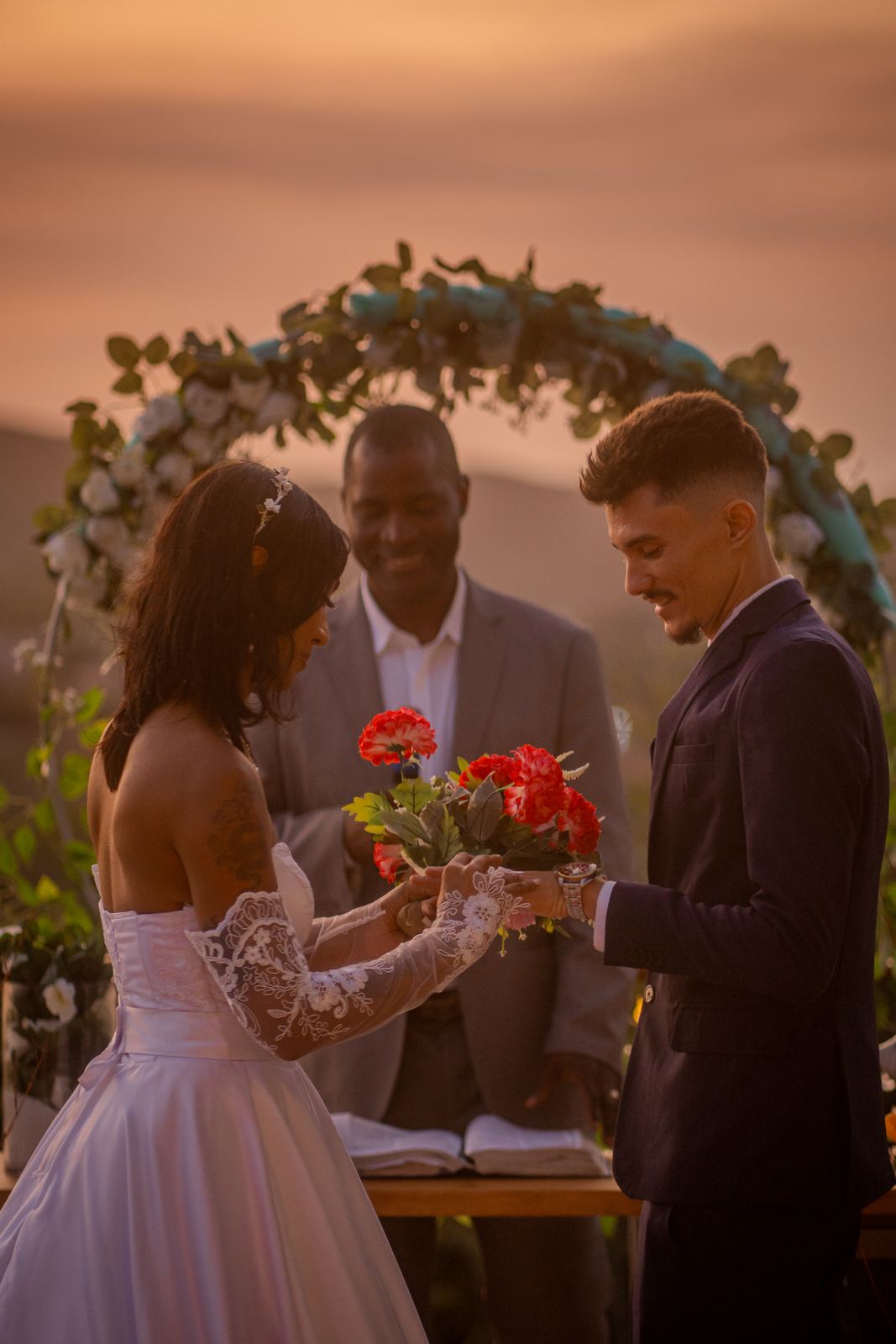 Cerimônia de casamento ao pôr do sol sob arco de flores