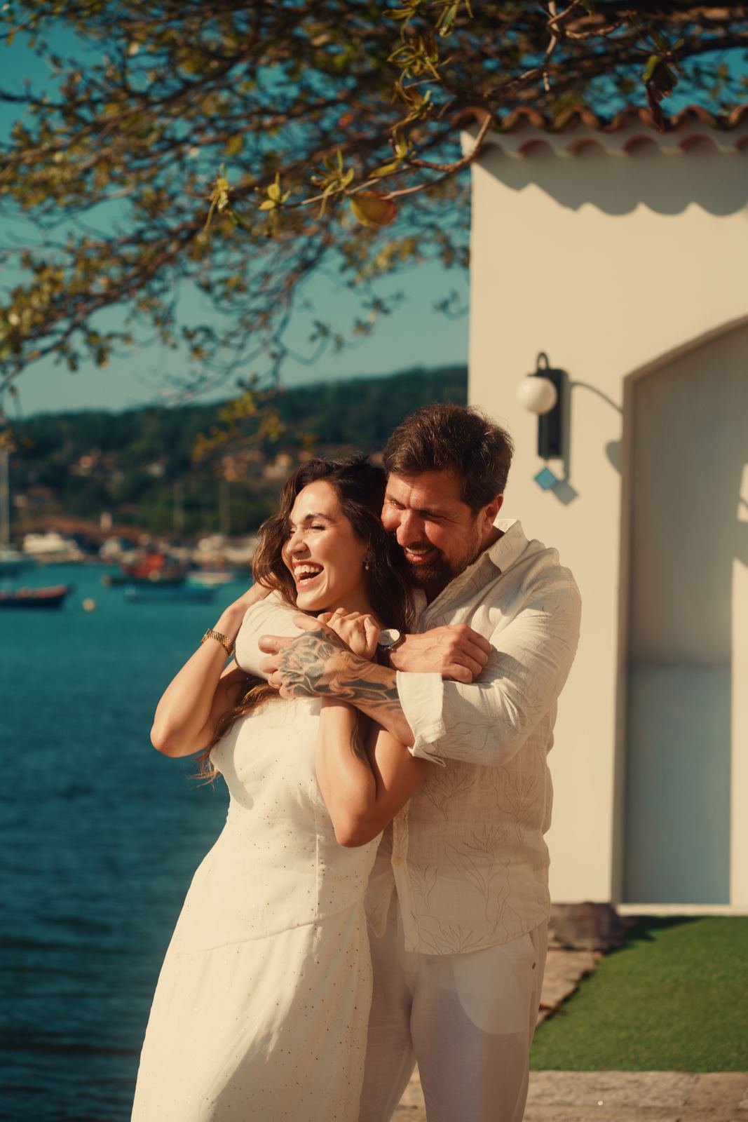 Casal abraçado e sorrindo em frente à baía