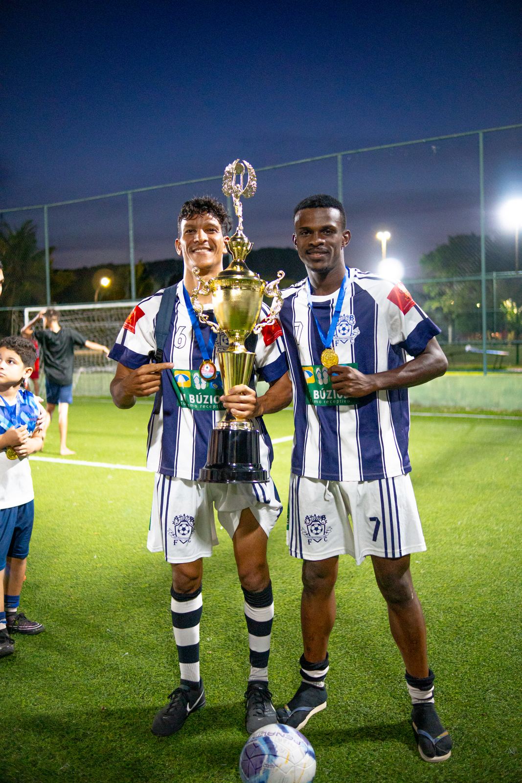 Jogadores com troféu no campo à noite